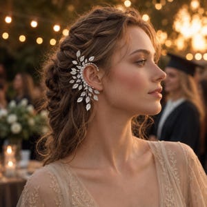 May include: A silver-toned ear cuff featuring a delicate, branching design adorned with numerous small, sparkling clear crystals shaped like leaves. The piece wraps around the outer edge of the ear, extending upwards and downwards in a vine-like pattern.