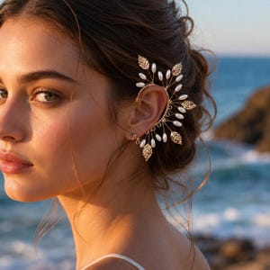 May include: A gold ear cuff featuring leaf and pearl accents. The ear cuff wraps around the ear and includes a small stud earring. The design incorporates gold-colored leaves and white pearls, creating an elegant and nature-inspired look.