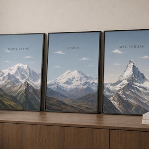 May include: Three framed vertical wall art prints featuring mountain landscapes. The left print is labelled Mont Blanc, the centre print is labelled Elbrus, and the right print is labelled Matterhorn. Each print shows snow-capped peaks under a blue sky.