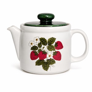 Peut inclure: Une théière en céramique blanche dotée d'un couvercle vert foncé brillant avec un bouton de préhension. Le corps de la théière est orné d'une illustration botanique représentant des fraises rouges, des feuilles vertes et des fleurs blanches.