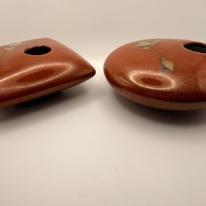May include: Two ceramic vases in a reddish-brown hue. One is rectangular with rounded corners, the other is oval. Both have a single opening and a subtle floral design. The vases have a glossy finish.