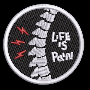 May include: A circular embroidered patch with a black background and a white border. It features a white human spine graphic, three red lightning bolt symbols on the left, and the white embroidered text "LIFE IS PAIN" on the right side.