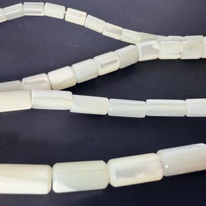 Peut inclure: Gros plan sur des rangées de perles rectangulaires blanc cassé. Les perles ont un léger éclat et sont enfilées, créant des lignes courbes. Les perles sont de taille et de forme uniformes, pour la création de bijoux ou d'autres travaux manuels.