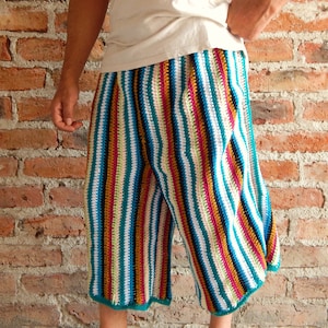 May include: Multicoloured striped crochet trousers with a teal trim. The trousers are made with a variety of colours, including white, black, red, yellow, and green.