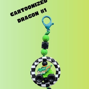 K&ouml;nnte beinhalten: Ein Cartoon-Drachen-Schl&uuml;sselanh&auml;nger in Gr&uuml;n und Schwarz. Der Drache befindet sich in einem schwarz-wei&szlig; karierten Kreis. Der Schl&uuml;sselanh&auml;nger hat einen blauen Verschluss und ist mit gr&uuml;nen und schwarzen Perlen verziert. Der Text auf dem Bild lautet "Cartoonized Dragon #1".