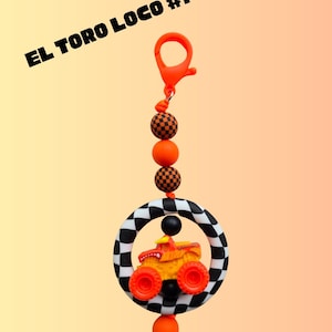 K&ouml;nnte beinhalten: Ein Schl&uuml;sselanh&auml;nger mit einem Monster-Truck-Design. Der Truck ist orange und gelb, eingebettet in einen schwarz-wei&szlig; karierten Ring. Der Schl&uuml;sselanh&auml;nger enth&auml;lt orangefarbene Perlen und einen Verschluss, mit dem Text "EL TORO LOCO #1".