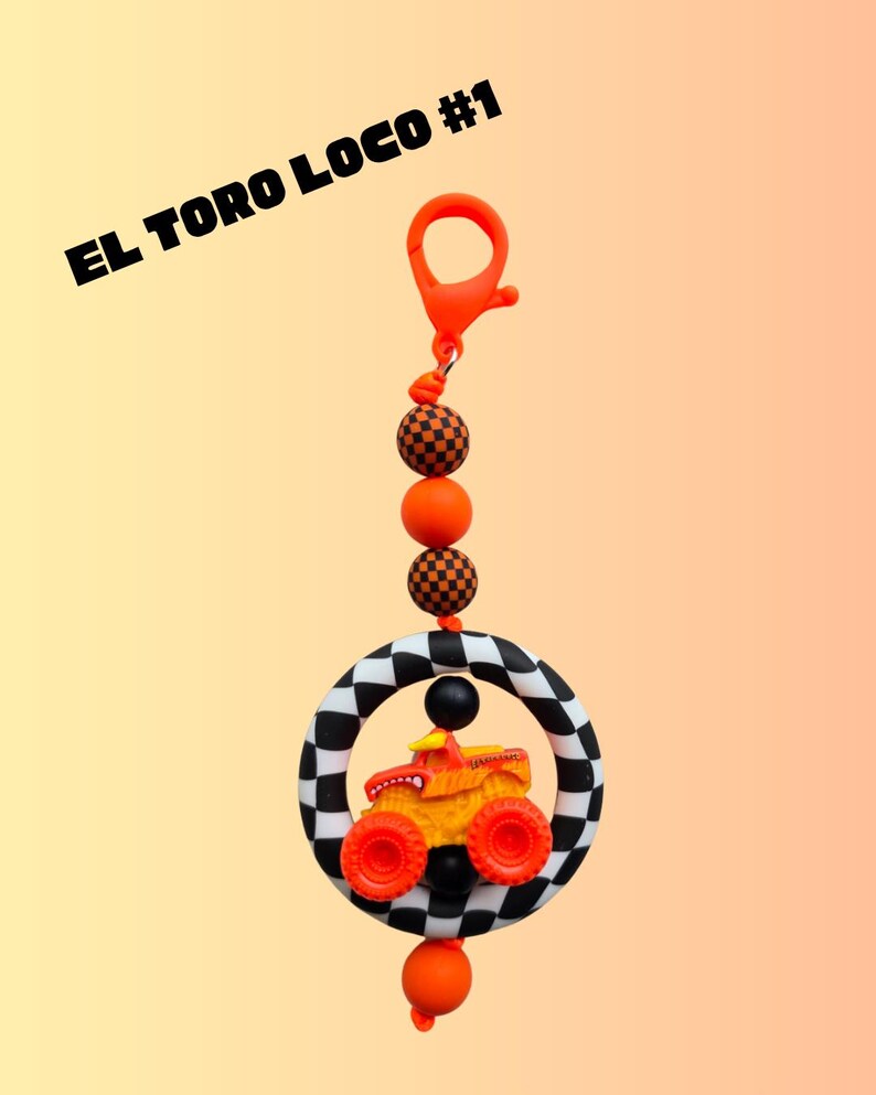 K&ouml;nnte beinhalten: Ein Schl&uuml;sselanh&auml;nger mit einem Monster-Truck-Design. Der Truck ist orange und gelb, eingebettet in einen schwarz-wei&szlig; karierten Ring. Der Schl&uuml;sselanh&auml;nger enth&auml;lt orangefarbene Perlen und einen Verschluss, mit dem Text "EL TORO LOCO #1".