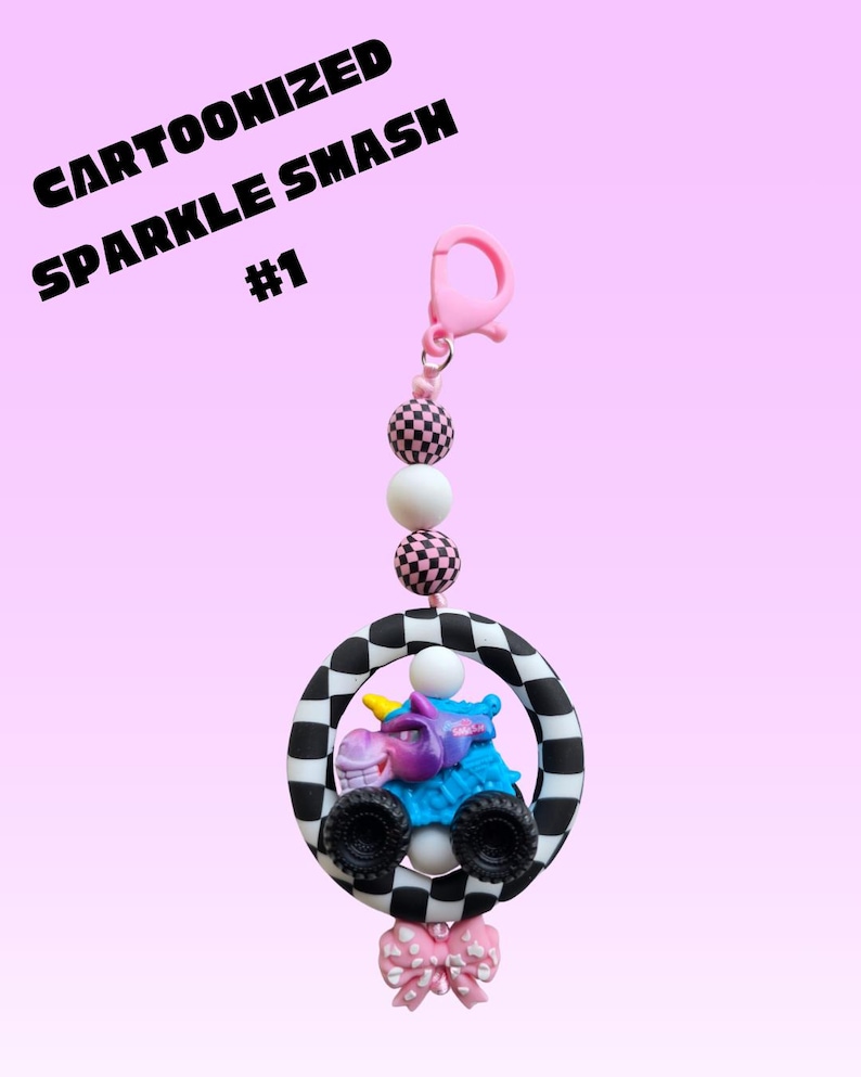 K&ouml;nnte beinhalten: Ein Cartoonized Sparkle Smash Schl&uuml;sselanh&auml;nger mit einem rosa Verschluss, karierten Perlen und einem Cartoon-Monster-Truck in einem schwarz-wei&szlig; karierten Kreis. Unten befindet sich eine rosa Schleife. Der Text "Cartoonized Sparkle Smash #1" steht oben.