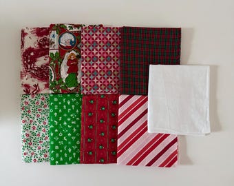 Può includere: Una collezione di nove quadrati di tessuto piegati con vari motivi a tema natalizio, tra cui toile rosso e bianco, una stampa con angelo, forme geometriche, tartan verde e rosso, motivi floreali, icone verdi, ornamenti rossi e righe.