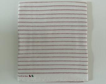 Può includere: Un panno in tessuto bianco con strisce orizzontali composte da sottili linee alternate rosse e verdi. Nell'angolo in basso a sinistra, il testo recita "d world out there." accompagnato da piccole sagome di conigli rossi e verdi.