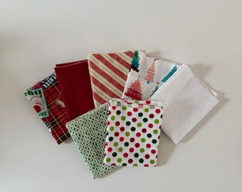 Può includere: Una collezione di sette quadrati di tessuto piegati con vari motivi, tra cui pois rossi e verdi, strisce diagonali rosse e bianche, alberi di Natale, un tartan rosso con motivi di Babbo Natale, tessuto rosso tinta unita e bianco tinta unita.