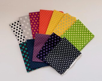Può includere: Una collezione di dodici campioni di tessuto rettangolari disposti a ventaglio. Ogni pezzo di tessuto presenta uno sfondo di colore solido distinto con un motivo ripetuto di pois bianchi o colorati a contrasto di varie dimensioni.
