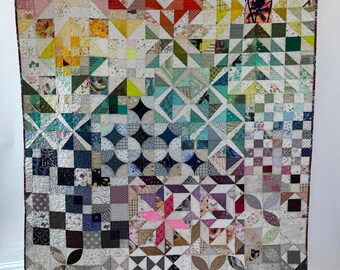 Può includere: Una grande trapunta rettangolare caratterizzata da un vivace design patchwork composto da numerosi piccoli quadrati e triangoli di tessuto. Il tessuto mostra uno spettro di colori che include rosso, arancione, giallo, verde, blu, viola e motivi in bianco e nero.
