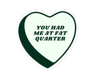 Può includere: Un adesivo a forma di cuore con un centro verde menta pallido e un bordo verde bosco scuro. Il testo 'YOU HAD ME AT FAT QUARTER' è stampato in lettere maiuscole verde bosco scuro al centro del cuore, con un carattere serif in grassetto.