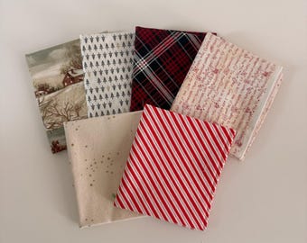 Può includere: Una collezione di sei quadrati di tessuto piegati con vari motivi, tra cui un paesaggio invernale, piccoli alberi verdi su bianco, tartan rosso e nero, strisce rosso e bianco, stelle dorate su crema e stampe con testi natalizi.
