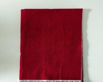 Può includere: Un pezzo rettangolare di tessuto rosso scuro con un aspetto intrecciato e testurizzato. Il bordo inferiore presenta una cimosa bianca stampata con il testo nero: Rustic weave by moda modafabrics.com made in.