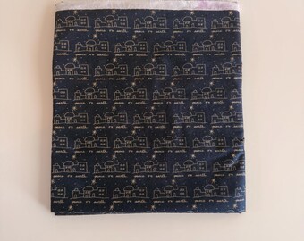 Può includere: Un pezzo di tessuto rettangolare blu navy scuro con un motivo ripetuto di edifici, stelle e il testo "peace on earth" stampato in bianco con un carattere corsivo. Il tessuto presenta un bordo superiore ripiegato con una rifinitura viola chiaro.