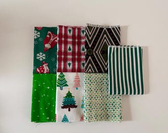 Può includere: Una collezione di sette quadrati di tessuto piegati con vari motivi, tra cui Babbo Natale, quadri rossi e bianchi, forme geometriche nere e bianche, strisce verdi e bianche, stelle, alberi di Natale e rombi verdi.