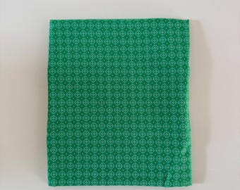 Può includere: Un pezzo di tessuto verde piegato con un motivo geometrico ripetitivo di piccole croci e punti bianchi disposti a griglia. Il tessuto presenta un colore di base verde smeraldo uniforme con una stampa bianca simmetrica e nitida.