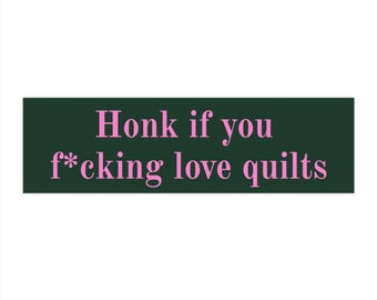 Può includere: Un adesivo rettangolare verde scuro con il testo rosa "Honk if you f*cking love quilts" in un carattere serif. Il design è centrato sull'adesivo, con la frase disposta su due righe contro lo sfondo di colore verde scuro uniforme.