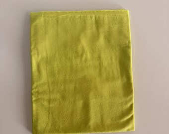 Può includere: Un pezzo rettangolare di tessuto verde lime piegato in una forma piatta e ordinata. Il tessuto presenta una superficie liscia e opaca con pieghe orizzontali e verticali visibili dovute al processo di piegatura, mostrando un colore solido.
