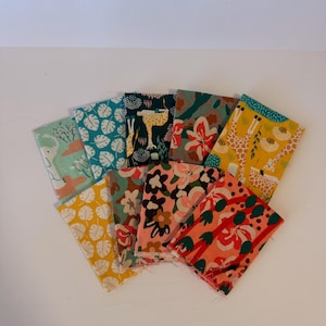 May include: A collection of nine rectangular fabric swatches arranged in a fan shape. The patterns include various colorful prints featuring elephants, giraffes, tropical leaves, and floral motifs in shades of yellow, teal, pink, and green.