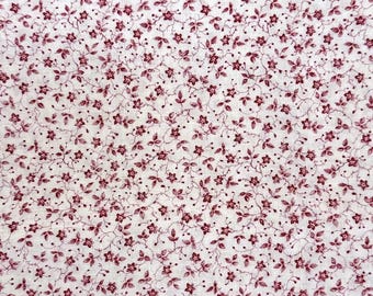 Può includere: Un tessuto bianco caratterizzato da un motivo denso e ripetitivo di piccoli fiori rosso scuro e sottili viticci delicati. La stampa floreale è distribuita uniformemente su tutta la superficie, creando un design botanico coerente.