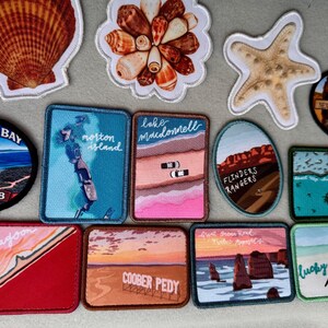May include: A collection of embroidered patches featuring various Australian landmarks and coastal themes, including a seashell, starfish, and rectangular patches depicting locations like Bremer Bay, Lake MacDonnell, Coober Pedy, and Lucky Bay.