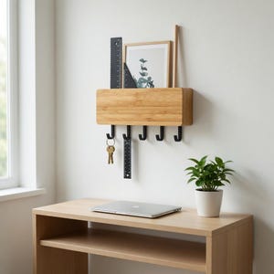May include: A wooden wall-mounted organizer with black hooks, a small framed picture, and a ruler. The organizer has a natural wood finish and includes a small plant in a white pot. A laptop sits on a wooden desk below.