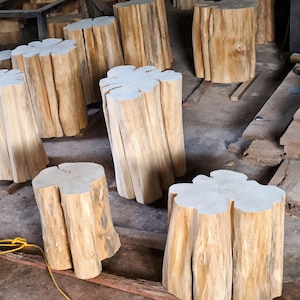 May include: A collection of light brown wooden tree stump stools with natural vertical grain patterns and flat, circular tops. Each piece is crafted from a solid log, showcasing the raw texture of the bark and the light-coloured wood grain.
