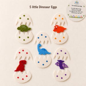 May include: Five felt dinosaur eggs with white shells featuring colorful polka dots. Each egg is cracked open to reveal a different felt dinosaur: a green stegosaurus, orange triceratops, blue brachiosaurus, red tyrannosaurus, and purple pterodactyl.