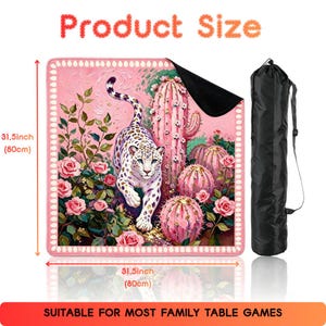 May include: A square game mat measuring 31.5 inches by 31.5 inches, featuring a pink-toned illustration of a leopard among roses and cacti, with a black carrying bag. The text Product Size and SUITABLE FOR MOST FAMILY TABLE GAMES is visible.
