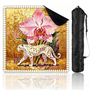 May include: A square mat featuring an impasto-style painting of a white leopard with gold spots walking beneath a large pink orchid against a textured gold background, bordered by a white scalloped edge, accompanied by a black cylindrical carrying bag.