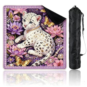 May include: A square mat featuring a white leopard cub with black spots, wearing a gold collar, surrounded by purple lotus flowers, gold butterflies, and pearl jewelry accents, accompanied by a black cylindrical carrying bag with a strap.