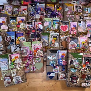 May include: A collection of rectangular book bundles wrapped in brown paper with floral patterns. Each bundle is tied with ribbon and decorated with various colorful stickers featuring book-related text and illustrations, including phrases like Book Nerd.