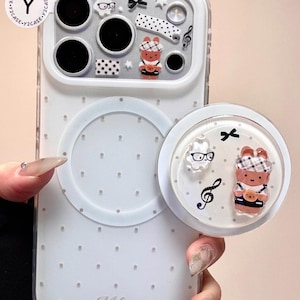 Könnte beinhalten: Transparente Handyhülle mit weißem Polka-Dot-Muster und passendem Pop-Socket. Die Hülle hat dekorative Elemente wie einen Bären, Noten und eine Schleife. Der Name "Melanie" ist auf der Hülle aufgedruckt.