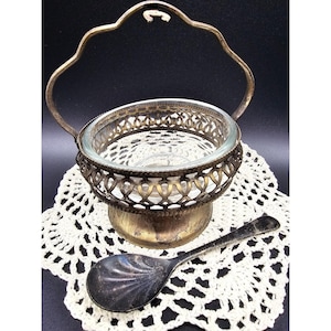 May include: A clear glass bowl set in a tarnished brass-toned metal frame with a scalloped handle and a matching tarnished metal spoon featuring a shell-shaped bowl. The metal components exhibit a weathered, aged patina throughout the entire set.