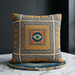 May include: Square decorative pillow with an eye design. The pillow features a mustard yellow background with a geometric pattern in navy blue and cream. The center of the pillow has a blue eye design with orange accents.