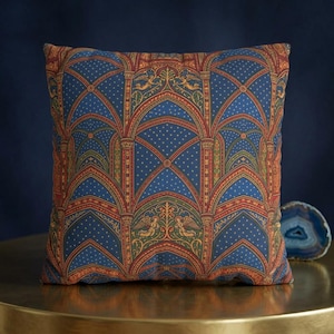 May include: A square throw pillow featuring a repeating architectural pattern of blue gothic arches with red and gold accents. The design includes small gold dots on a blue background and stylized angel figures integrated into the structural motifs.