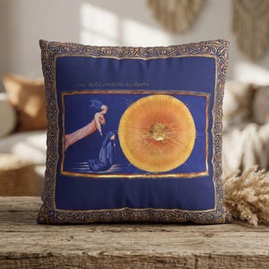 May include: Square cushion with a dark blue backdrop and a gold ornate border. The cushion features a central image of a large orange circle with figures and text. The text reads "come della comitella ti colloca".
