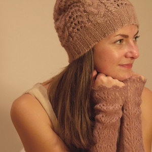 May include: A woman wearing a light brown knitted hat and matching fingerless gloves. The hat has a delicate lace pattern and the gloves have a similar design.