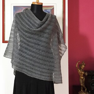 May include: A gray knitted shawl with a lacy pattern, draped over a black skirt on a mannequin.