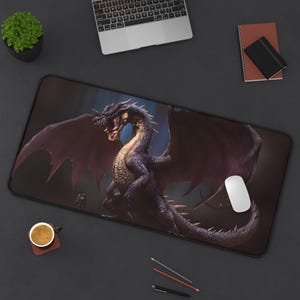 Puede incluir: Alfombrilla de ratón rectangular con una ilustración detallada de un dragón púrpura con las alas extendidas. El dragón tiene dientes y garras afiladas. La alfombrilla está sobre una superficie oscura con un portátil, una taza de café y otros suministros de oficina.
