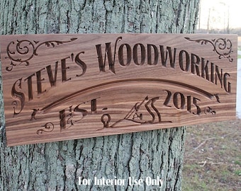 May include: A wooden sign with the text "STEVE'S WOODWORKING EST. 2015" carved into it. The sign is made of walnut wood and has a dark brown color.