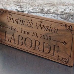 May include: A wooden sign with the text "Justin & Jessica - Est. June 20, 2009 - LABORDE" engraved in a decorative font.