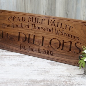 May include: A wooden sign with a Celtic knot design and the text "CÉAD MILE FÁILTE One Hundred Thousand Welcomes The DILLONS Est. June 8, 2003".