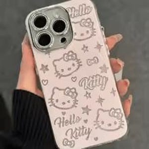 Puede incluir: Una funda de tel&eacute;fono rosa claro con un anillo de c&aacute;mara plateado. La funda presenta m&uacute;ltiples ilustraciones del personaje Hello Kitty, estrellas y las palabras "Hello Kitty" en una fuente l&uacute;dica.