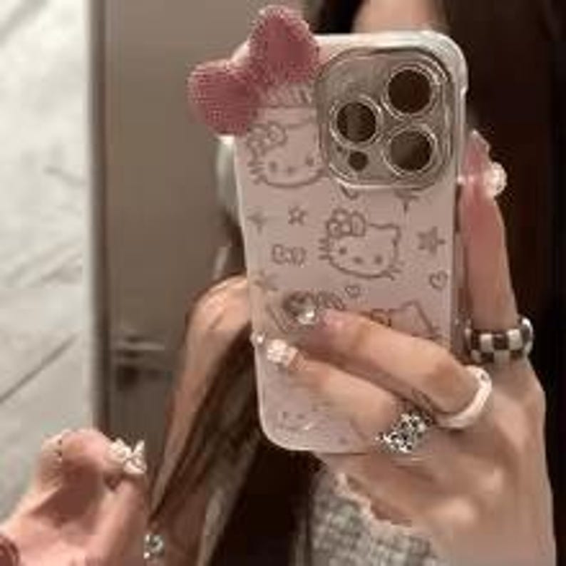 Puede incluir: Una funda transparente para tel&eacute;fono con un dise&ntilde;o de Hello Kitty rosa claro y un lazo a juego. La funda tiene un borde transparente y un patr&oacute;n repetido de caras y estrellas de Hello Kitty.
