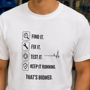 May include: A white crew neck t-shirt featuring black text and icons. The graphic displays four stacked squares with a magnifying glass, wrench, gear, and shield, followed by the text: FIND IT. FIX IT. TEST IT. KEEP IT RUNNING. THAT'S BIOMED.