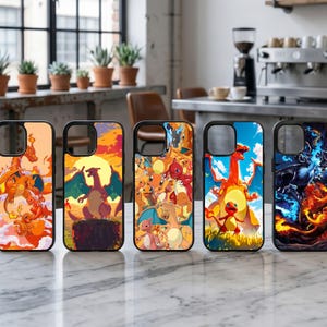 May include: Five phone cases with black borders and colorful illustrations. The designs feature various Pokémon characters in vibrant scenes with orange, red, and blue hues. The cases are displayed on a white marble surface.